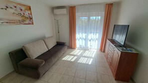 Ein Wohnzimmer mit einer Couch, einem Fernseher auf einer Holzkommode und einem Fenster mit Vorhängen.