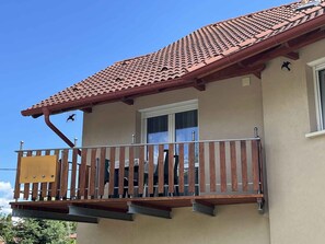 Ein Gebäude mit einem Ziegeldach, einem Balkon mit Holzgeländern und einem Fenster mit Vorhang.
