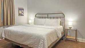 A bed with a metal frame, two bedside lamps, a wall-mounted picture, and wooden flooring. - 1 BD Near Ochsner | Quiet Courtyard Community (Jefferson)