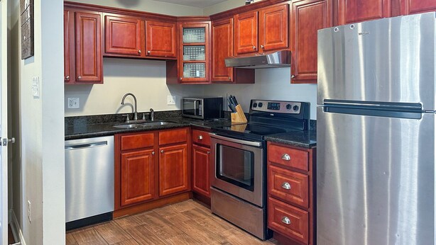 A kitchen with wooden cabinets, stainless steel appliances, and a tiled floor. - 1 BD Near Ochsner | Quiet Courtyard Community (Jefferson)