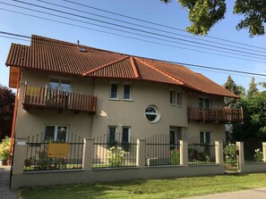 A two-story building with a tiled roof, balconies, and a fenced garden area. - Holiday apartment with air conditioning, Wi-Fi, parking and balcony (Zamárdi)