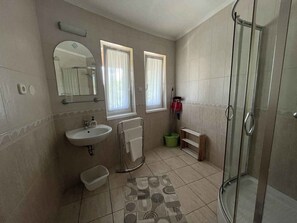 A bathroom with a sink, mirror, two windows with curtains, a shower, and a patterned floor. - Holiday apartment with air conditioning, Wi-Fi, parking and balcony (Zamárdi)