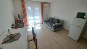 A living room with a sofa, a dining table with chairs, a TV, and a refrigerator. - Holiday apartment with Wi-Fi, air conditioning, balcony and parking (Zamárdi)