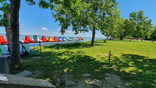 A grassy area with a row of colorful lounge chairs by a body of water. - Holiday apartment with Wi-Fi, air conditioning, balcony and parking (Zamárdi)