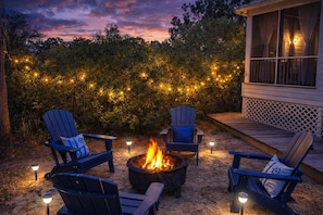 Eine Terrasse mit vier Adirondack-Stühlen, einer Feuerstelle und Lichterketten.