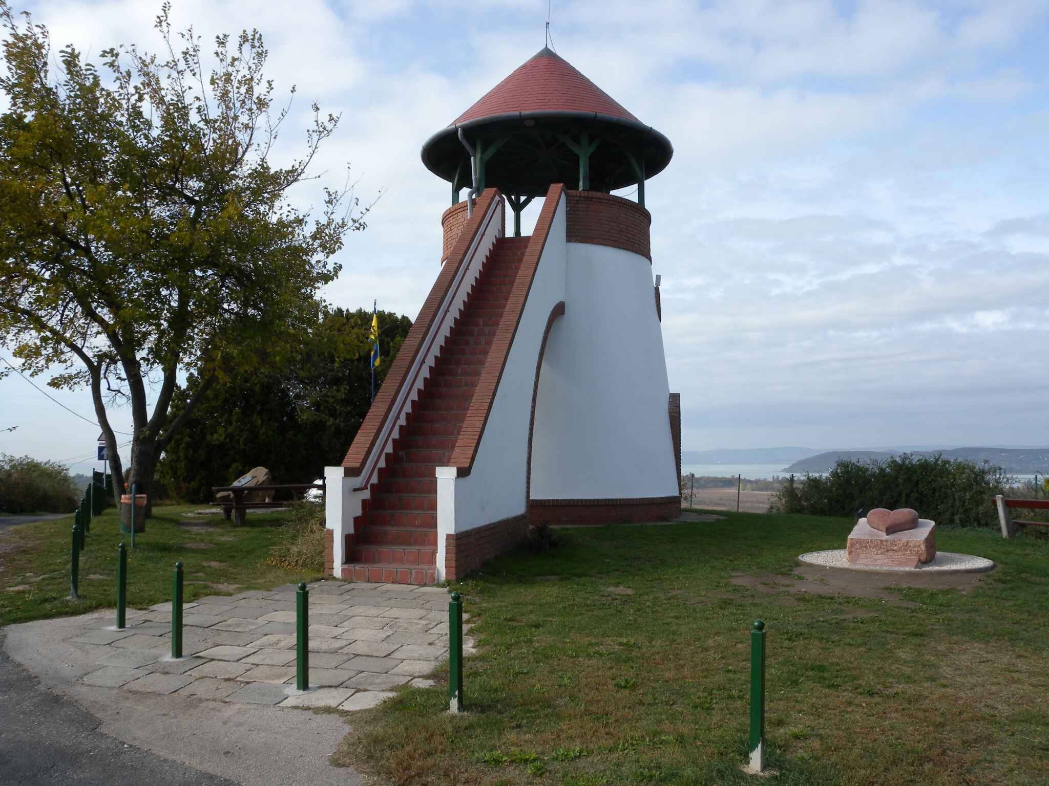 A conical tower with a staircase, surrounded by grass and trees, with a clear view of the sky and distant landscape.