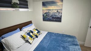 Ein Schlafzimmer mit einem Bett, einem Fenster mit Jalousien, einem an der Wand befestigten Bild und einer Deckenleuchte.