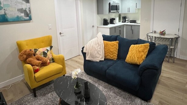 Ein Wohnzimmer mit einer Couch, einem Sessel, einem Couchtisch und einer Küche im Hintergrund.