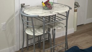 Ein kleiner Essbereich mit einem runden Tisch und zwei Stühlen, einer Obstschale auf dem Tisch und einem an der Wand befestigten Schild mit Wörtern wie 'breathe', 'relax' und 'sunwind'.