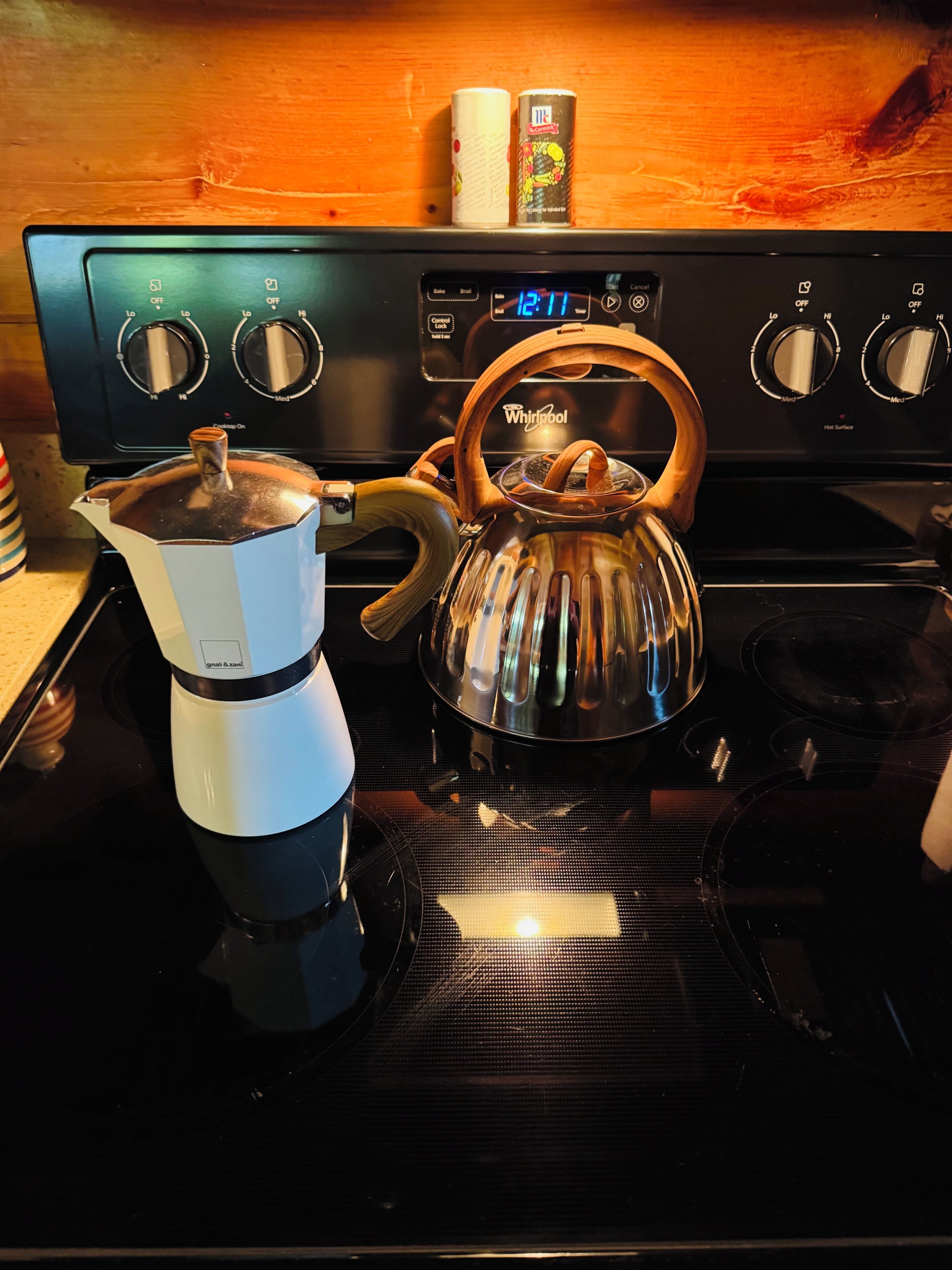 Een keuken met een koffiezetapparaat, waterkoker en een fornuis met bedieningsknoppen.