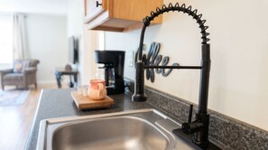 A kitchen with a modern faucet, a coffee maker, and a wooden cutting board with a jar and salt shakers.