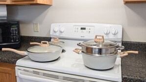 A kitchen with a white stove, two pots with wooden handles, a microwave, and wooden cabinets. - Convenient & Modern 2 Bed Apt Free Wi-Fi & Parking (Pikeville)