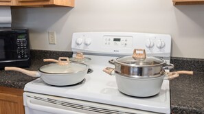 A kitchen with a white stove, two pots with wooden handles, a microwave, and wooden cabinets.