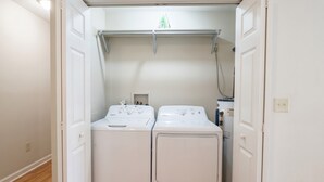 A laundry room with two front-loading washing machines, a metal drying rack, and a small shelf with items. - Convenient & Modern 2 Bed Apt Free Wi-Fi & Parking (Pikeville)