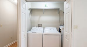 A laundry room with two front-loading washing machines, a metal drying rack, and a small shelf with items.