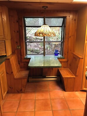 L’intérieur d’un chalet en bois, avec un banc, une table et une fenêtre donnant sur des rochers et des arbres.