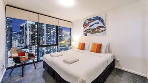 Una habitación de hotel con un ventanal grande, una cama, una silla y un cuadro en la pared.