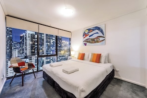 A hotel room with a large window, a bed, a chair, and a painting on the wall. - Exclusive Stays - Southpoint (Southbank)