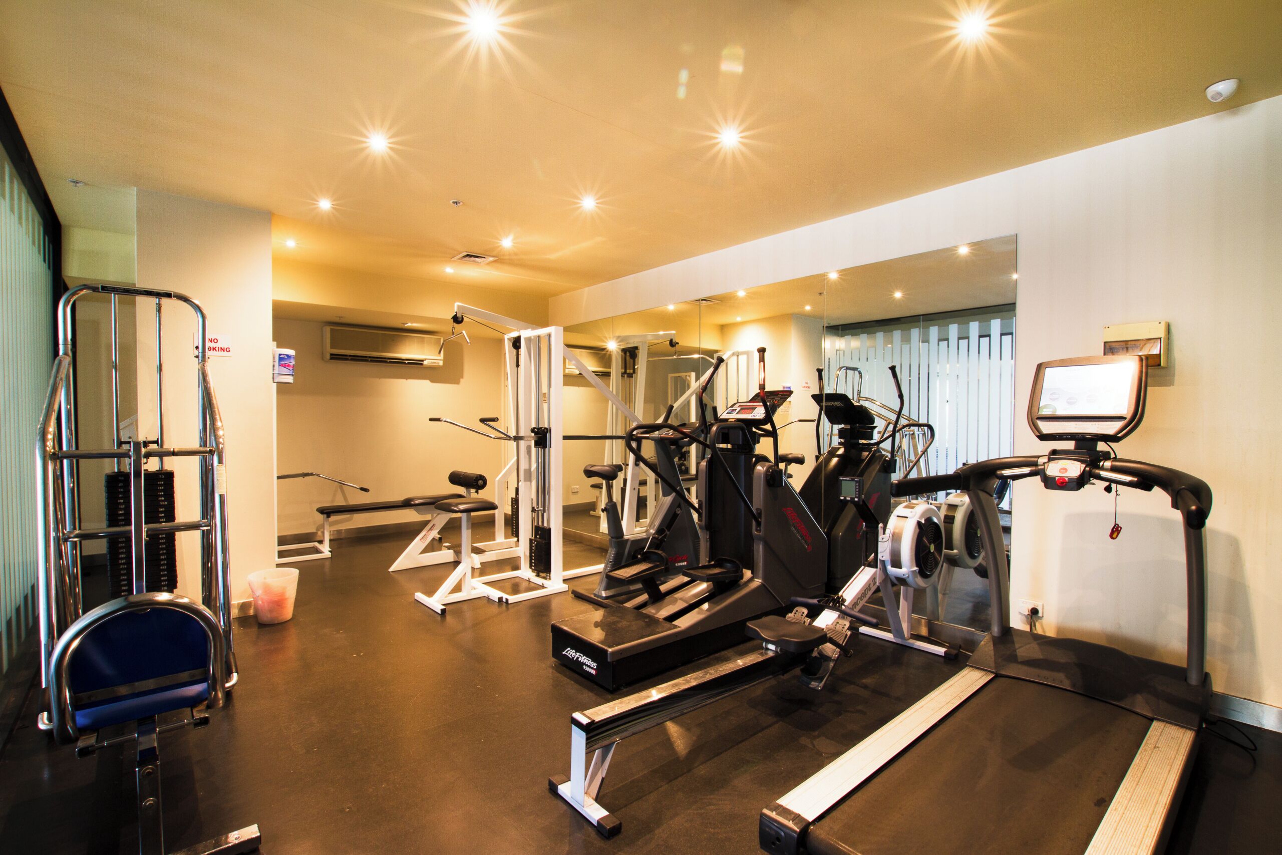 Una palestra con diverse attrezzature per esercizi, tra cui tapis roulant, macchinari per pesi e una sbarra per trazioni.