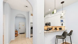 A modern kitchen with white cabinets, a granite countertop, and two black bar stools. - Family-Friendly Retreat Near Disney (Davenport)