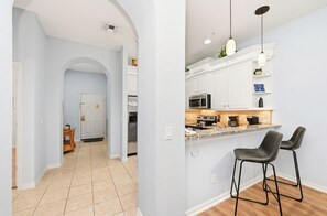 A modern kitchen with white cabinets, a granite countertop, and two black bar stools. - Family-Friendly Retreat Near Disney (Davenport)