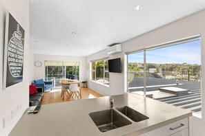 Eine moderne Küche mit einem großen Fenster, einem Essbereich mit Tisch und Stühlen sowie einem Wohnbereich mit Sofa und Fernseher.