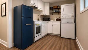 Een kleine keuken met een blauwe koelkast, witte kasten, een magnetron, een oven, en een witte wasmachine.
