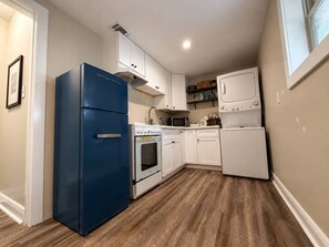 Eine kompakte Küche mit weißen Schränken, einem blauen Kühlschrank, einer Mikrowelle, einem Backofen und einem weißen Kühlschrank.