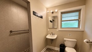 Een badkamer met douche, toilet, wastafel en een raam.