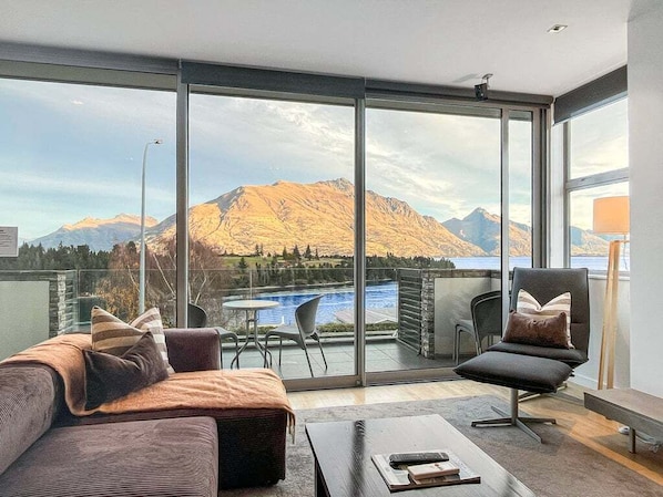 Ein modernes Wohnzimmer mit einer großen Schiebeglastür, die auf einen Balkon mit Blick auf Berge und einen See führt.