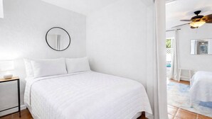 Un dormitorio con una cama, una mesita de noche, un espejo circular y un ventilador de techo.