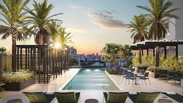 A rooftop pool with a city view, palm trees, and outdoor seating.