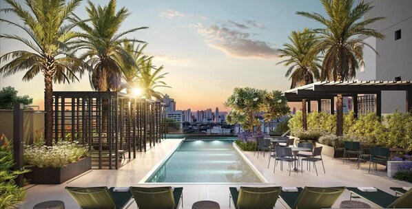 A rooftop pool with a city view, palm trees, and outdoor seating.