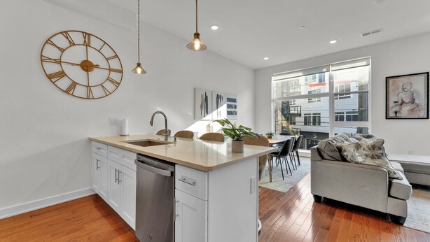 A modern kitchen with a central island, a dining area with a sofa, and a large window providing a view of the city. - Apartmint at Germantown Ave Philadelphia (Philadelphia)