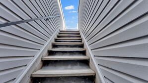 A staircase leading upwards between two buildings with white siding and a metal handrail. - Apartmint at Germantown Ave Philadelphia (Philadelphia)