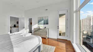 A modern bedroom with a large bed, a dresser, and a view of the city through a large window. - Apartmint at Germantown Ave Philadelphia (Philadelphia)