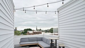 A rooftop patio with a gray sectional sofa, a small round table, and string lights. - Rooftop Bay Views - Downtown Lakehouse Sleeps 8 (Sandusky)