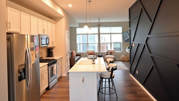 A modern kitchen with stainless steel appliances, a central island with bar stools, and a dining area with a view. - Rooftop Bay Views - Downtown Lakehouse Sleeps 8 (Sandusky)