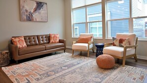 A living room with a brown leather sofa, two armchairs, a blue side table, and a patterned rug. - Rooftop Bay Views - Downtown Lakehouse Sleeps 8 (Sandusky)