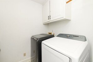 Ein Waschraum mit einer weißen Waschmaschine und einem Trockner, einem Schrank darüber und einer Holztür.