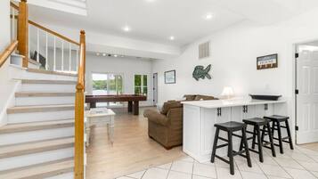 A spacious living area with a pool table, a brown sofa, and a kitchen area with bar stools.