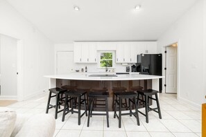 A modern kitchen with white cabinets, a black refrigerator, and a central island with bar stools. - Ultimate Lake House | Dock, Game Room, Sleeps 15 (Littleton)