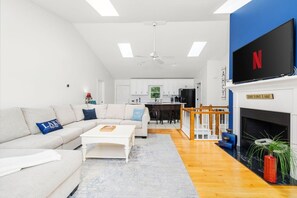 A modern living room with a sofa, coffee table, and a flat-screen TV mounted on the wall. - Ultimate Lake House | Dock, Game Room, Sleeps 15 (Littleton)