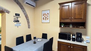 Un coin repas avec une table dressée pour six personnes, une cuisine équipée d’un four à micro-ondes et d’une machine à café, et une arche en briques.