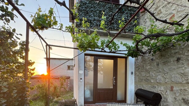 Une terrasse dotée de meubles en osier, d’un barbecue et d’une porte donnant accès à un bâtiment.