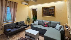 Un salon comprenant un canapé, une table basse, un tapis à motifs et un plafond avec des poutres apparentes.