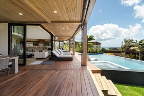 Et moderne udendørs opholdsområde med pool, træterrasse og havudsigt.
