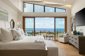 Ein Schlafzimmer mit einem großen Bett, einem Fernseher, einem Balkon mit Meerblick und einem Essbereich.