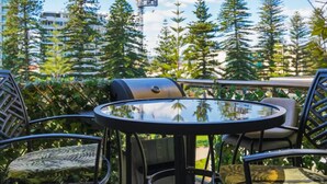 A patio with a round table and chairs, surrounded by greenery and tall trees. - Park View Hideaway (Glenelg)