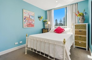 A bedroom with a bed, a nightstand, a dresser, a window with a view, and a painting on the wall. - Park View Hideaway (Glenelg)
